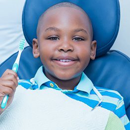 child smiling while holding a toothbrush during dental appointment