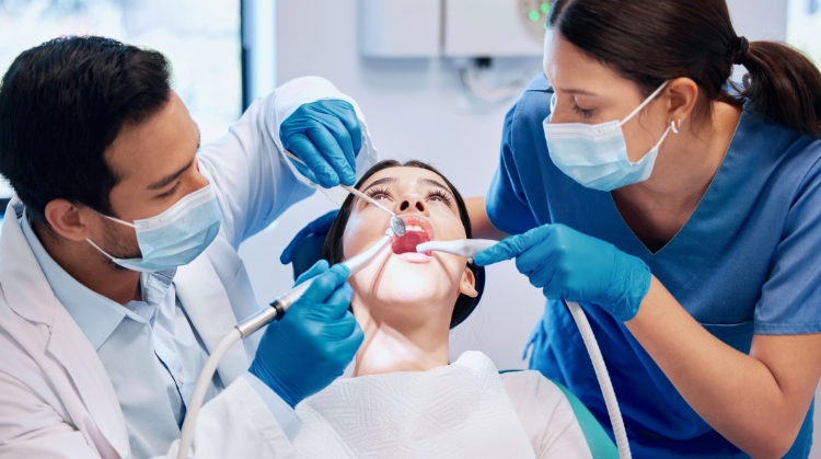 A dentist and dental assistant performing a wisdom teeth extraction on a patient in a dental clinic.